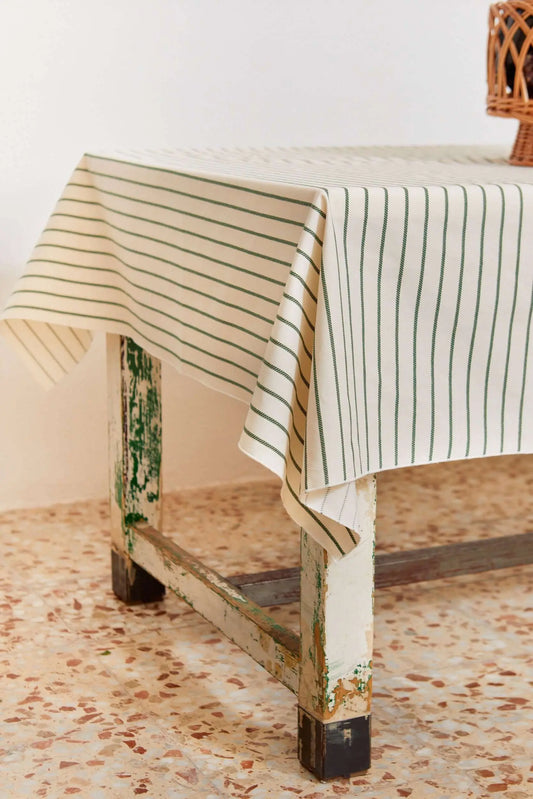 Off-white tablecloth with thin, vertical green chain-link stripes, draping over a rustic, distressed wooden table.