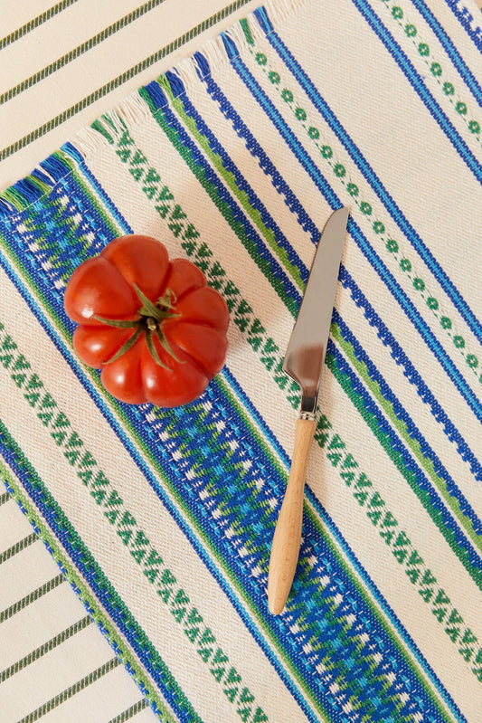 Pack de dos manteles individuales de algodón tejido con rayas y cenefas en tonos azules y verdes, con tomate y cuchillo.