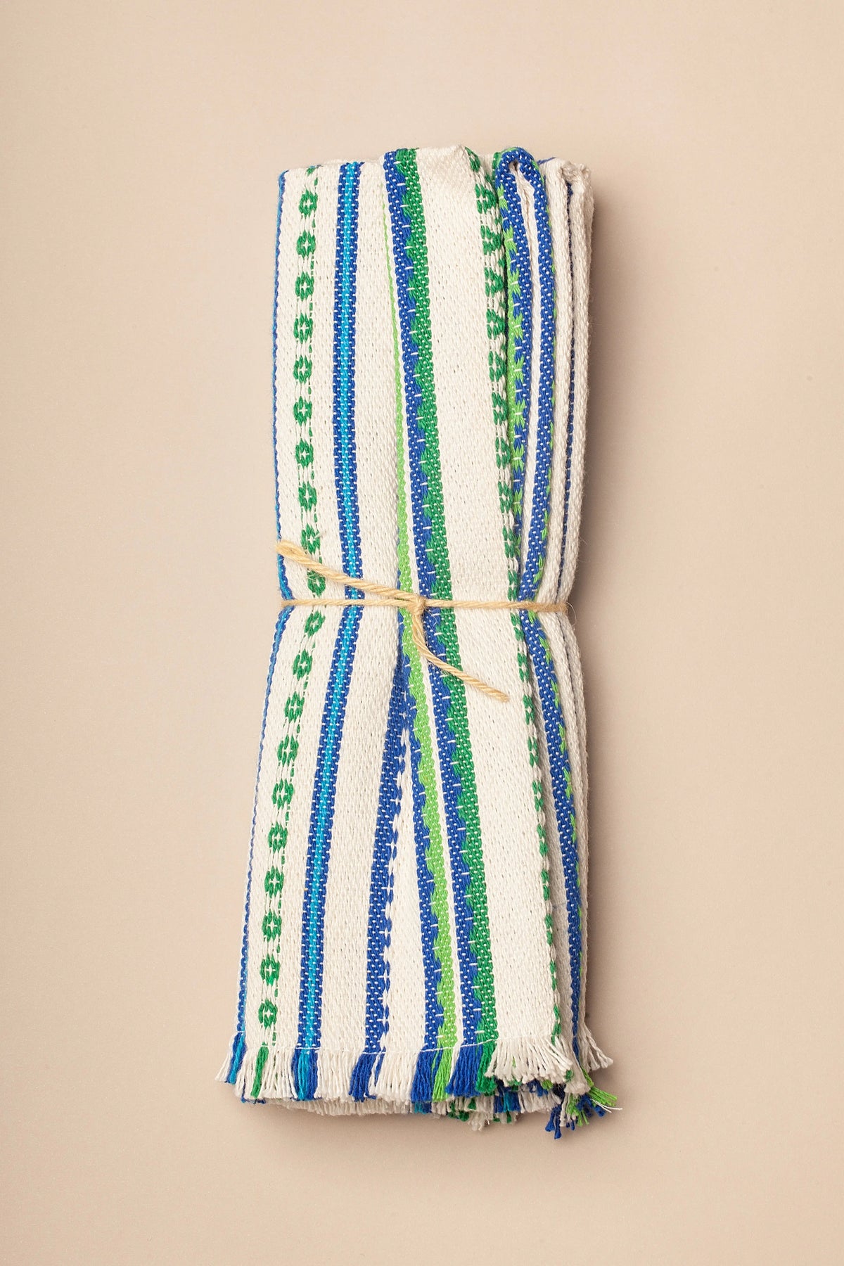 Pack of two folded woven placemats in off-white with blue and green vertical striped patterns and fringed edges.