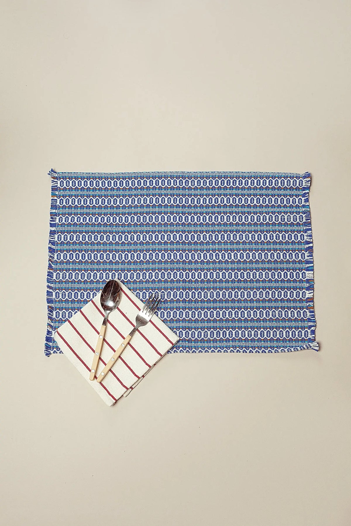 Mantel individual rectangular de tela azul con estampado retro ojo de perdiz, flecos y servilleta a rayas con cubiertos.