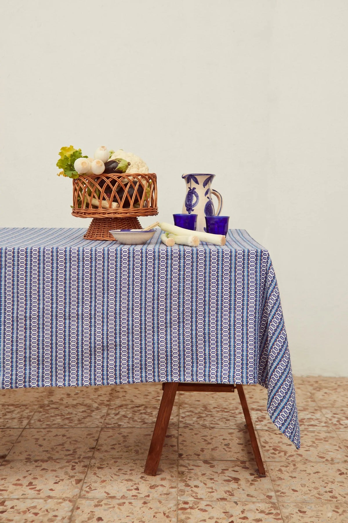 Mantel textil con estampado retro de pequeñas formas geométricas azules y blancas sobre mesa de madera.