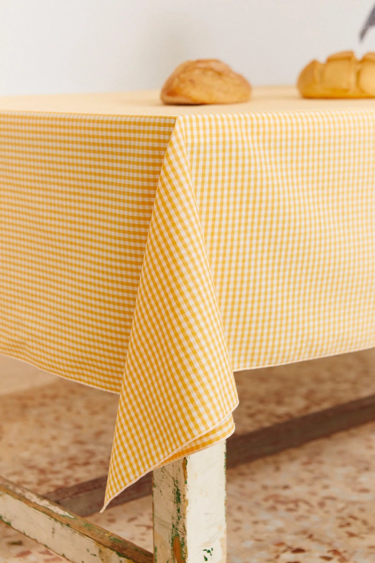 Mantel de tela con estampado de cuadros vichy en color amarillo, estilo rústico, cubriendo una mesa con pan encima.