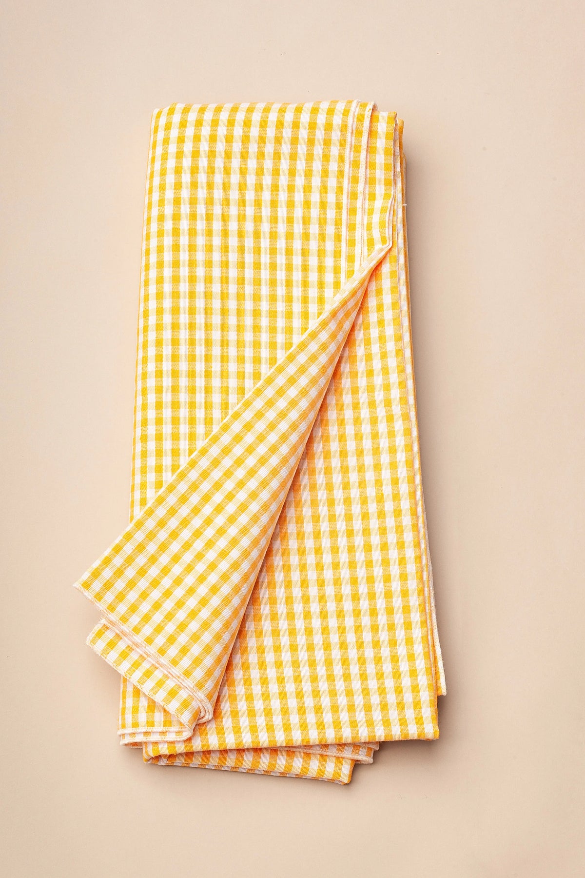 Mantel de tela con estampado de cuadros vichy en amarillo y blanco, plegado con un borde doblado sobre fondo neutro.