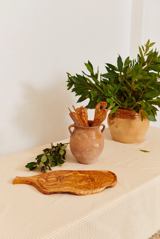 Mantel de tela con estampado de cuadros vichy en tono beige sobre una mesa decorada con objetos rústicos de madera.