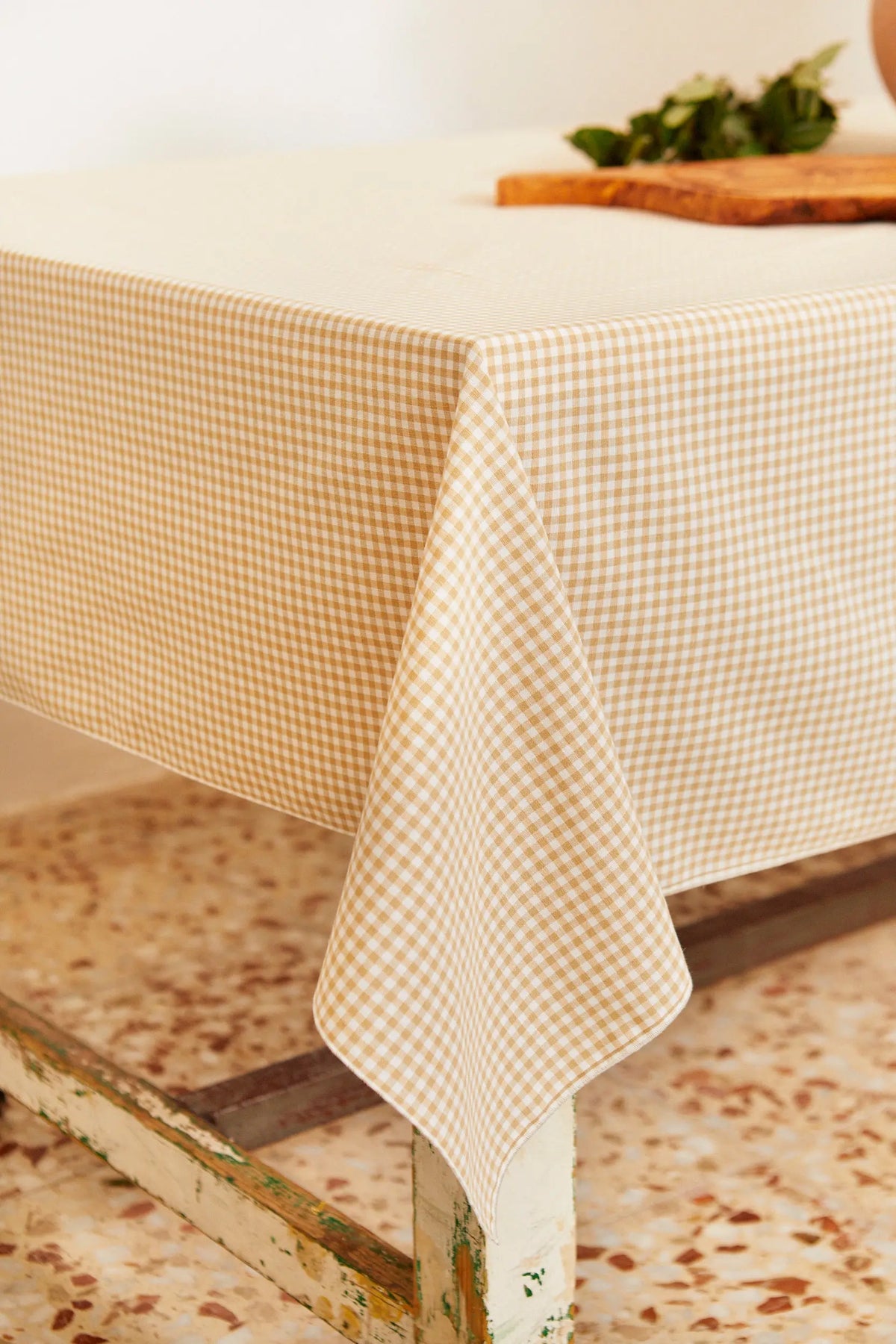 Mantel de estilo rústico con estampado de cuadros vichy en tonos beige y blanco sobre una mesa de madera.