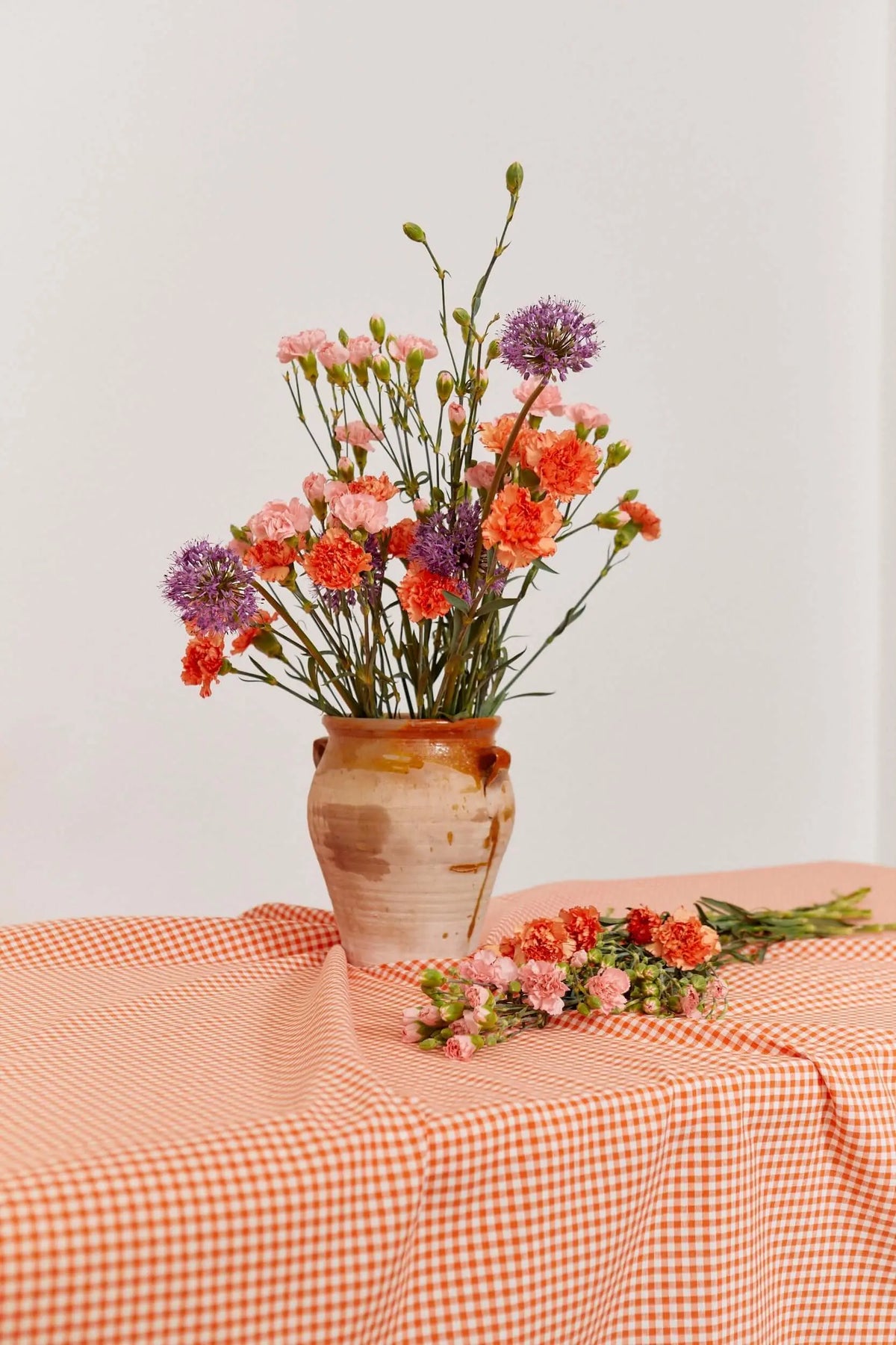 Mantel de tela con estampado de cuadros vichy en color naranja, sobre una mesa con flores en un jarrón de cerámica.