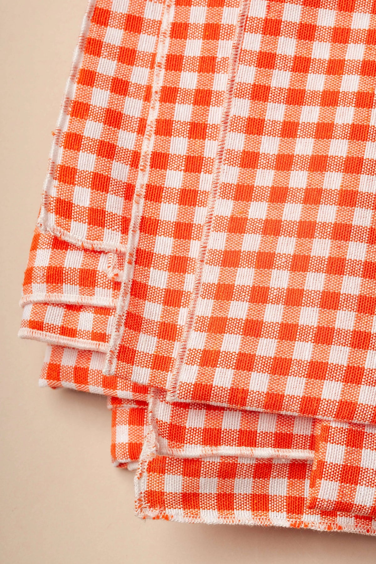 Mantel de tela con estampado de cuadros vichy en color naranja y blanco, con bordes deshilachados de estilo rústico.