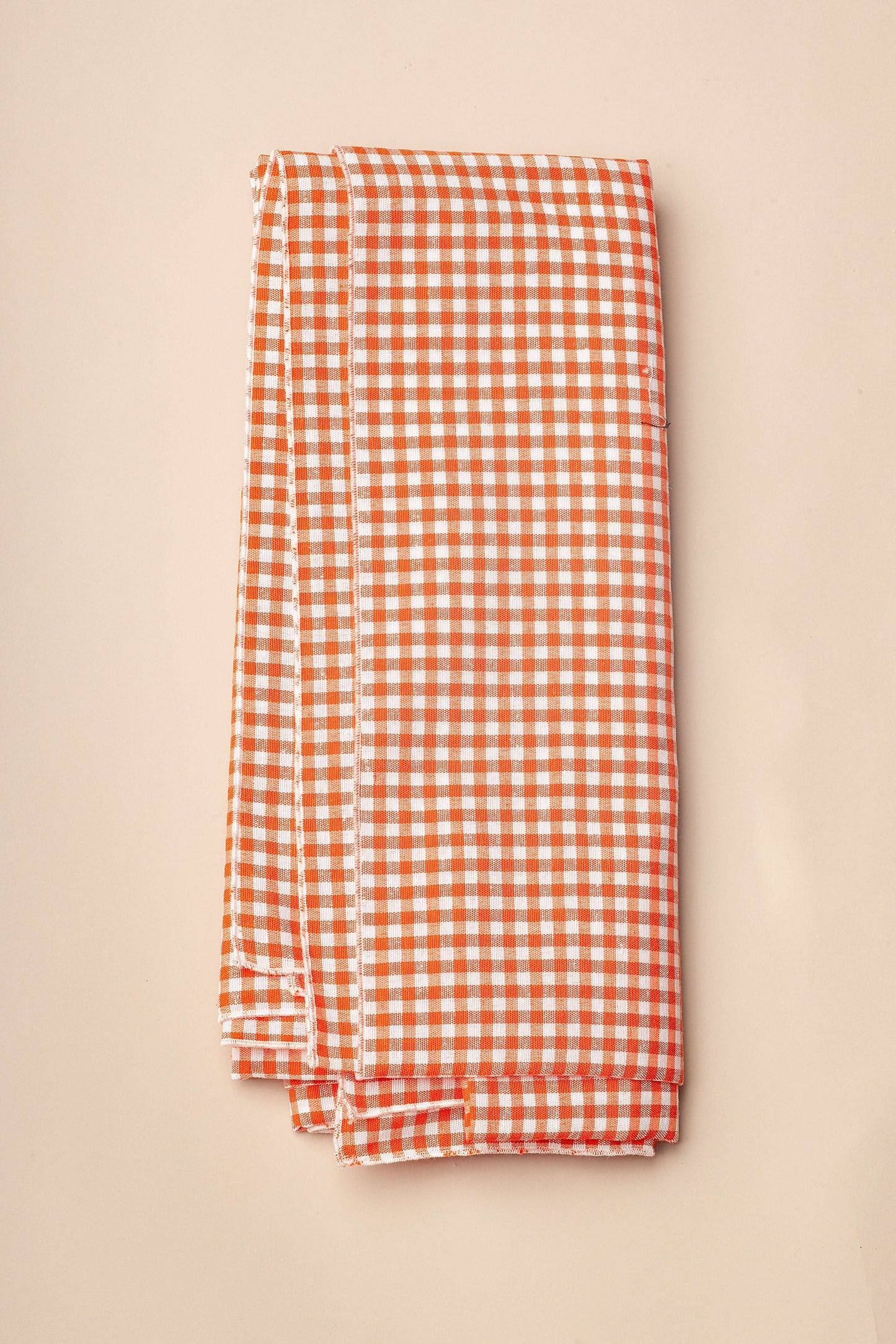 Mantel de tela con estampado de cuadros vichy en color naranja y blanco, doblado sobre fondo neutro.