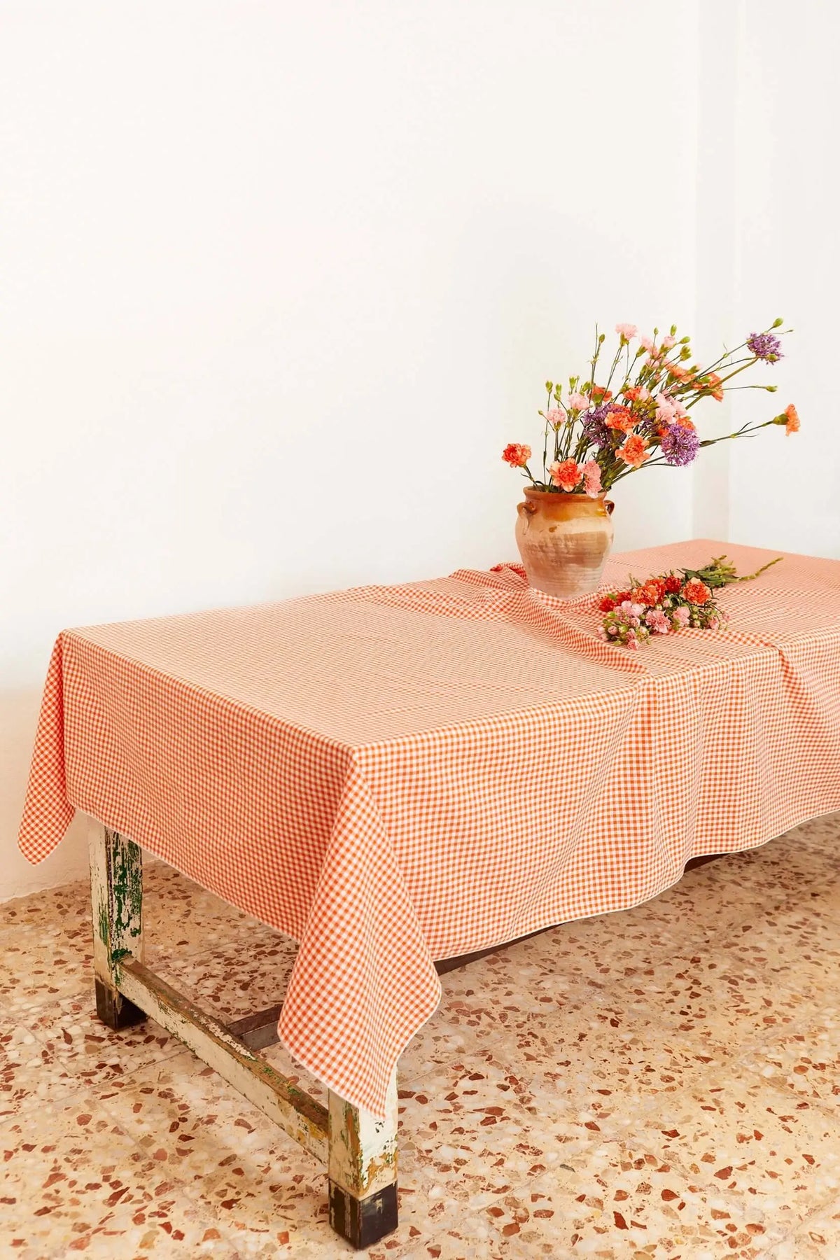 Orange and white gingham checkered tablecloth on a rustic table with a flower vase, indoors.