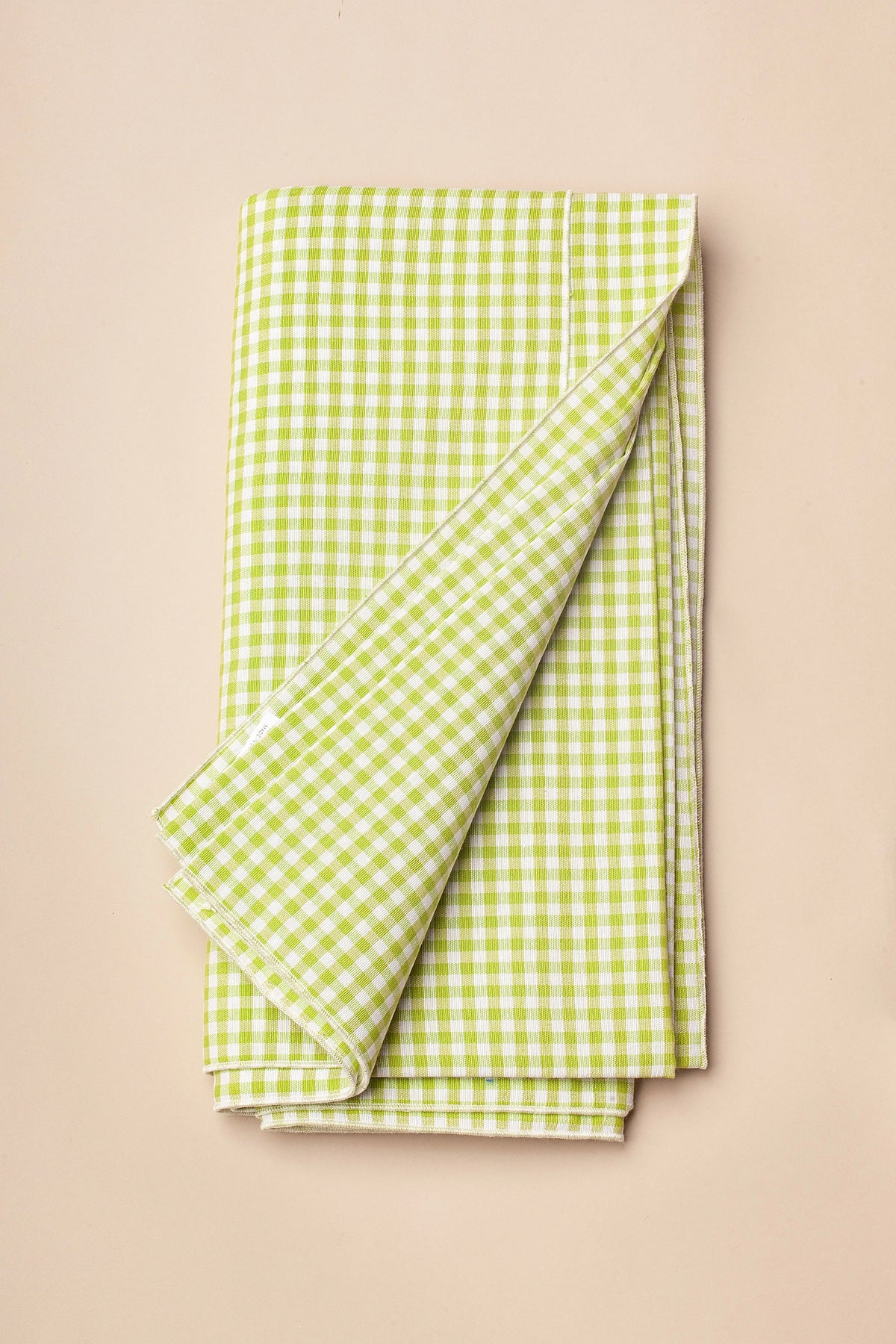 Mantel plegado de tela con estampado de cuadros vichy en color verde y blanco sobre fondo neutro.
