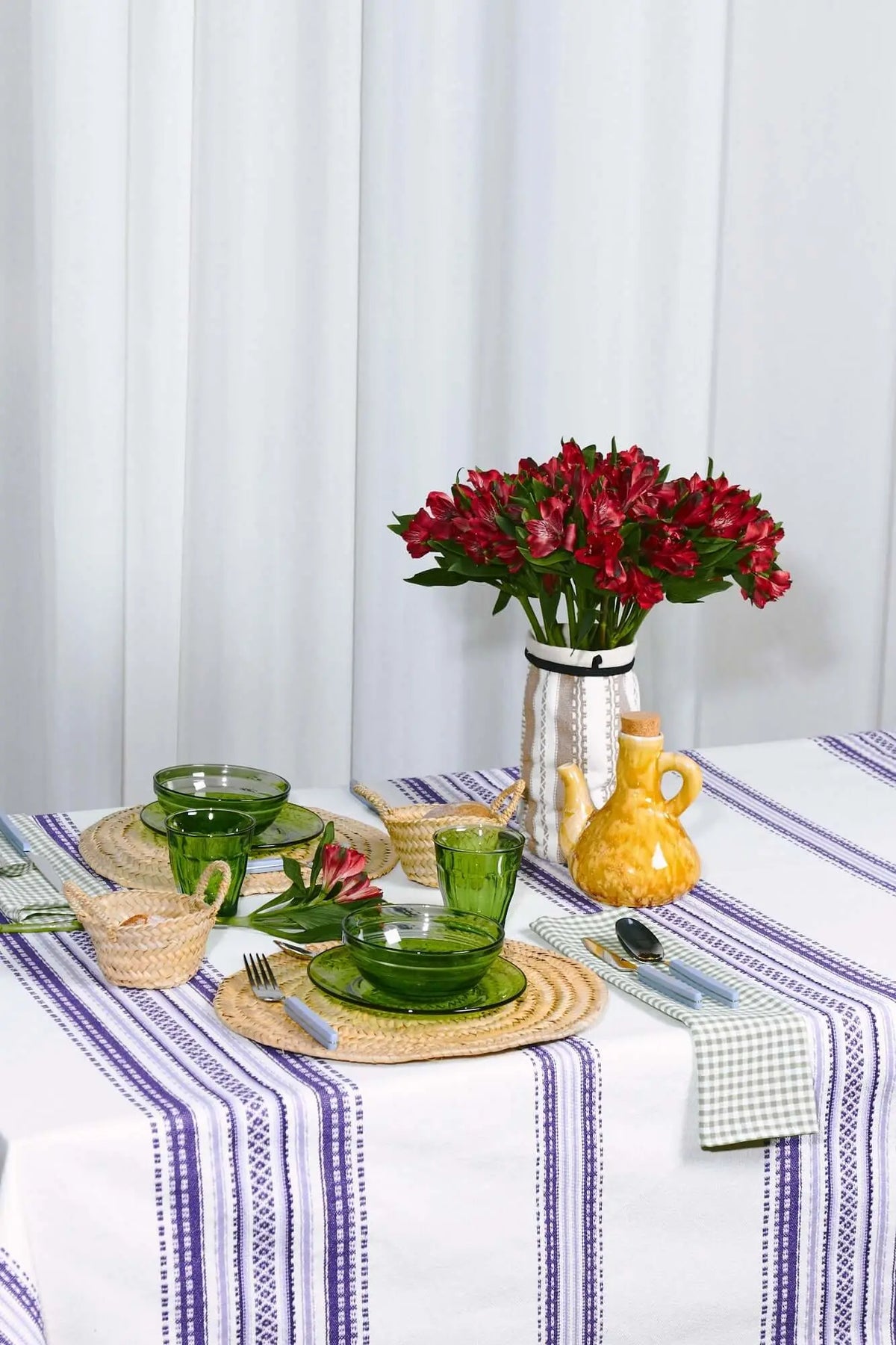 White tablecloth with mauve Alpujarra-style striped borders, set with green glassware and straw placemats.