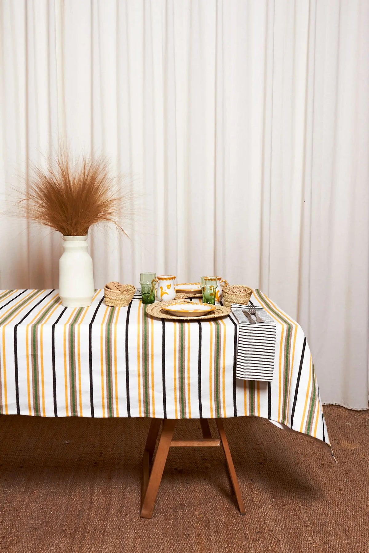 Tablecloth with vertical green, yellow, and black stripes on a white background, set with rustic woven tableware.