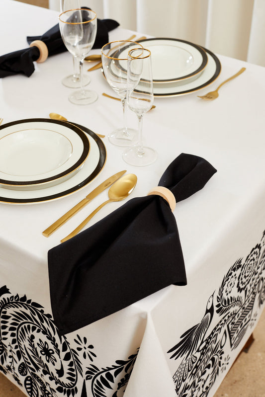 Pack de dos servilletas de loneta negra sobre mesa elegante con servilleteros de madera clara y vajilla sofisticada.