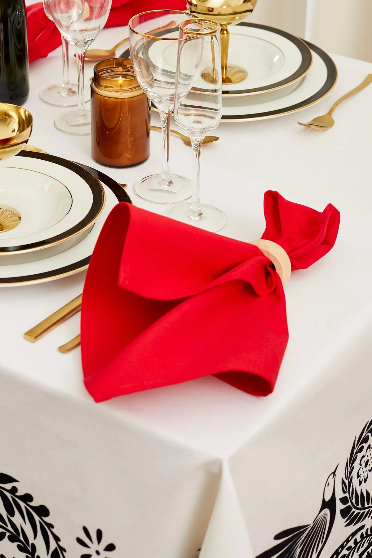 Bright red canvas napkin held by a wooden ring on a white table setting with plates and glasses.