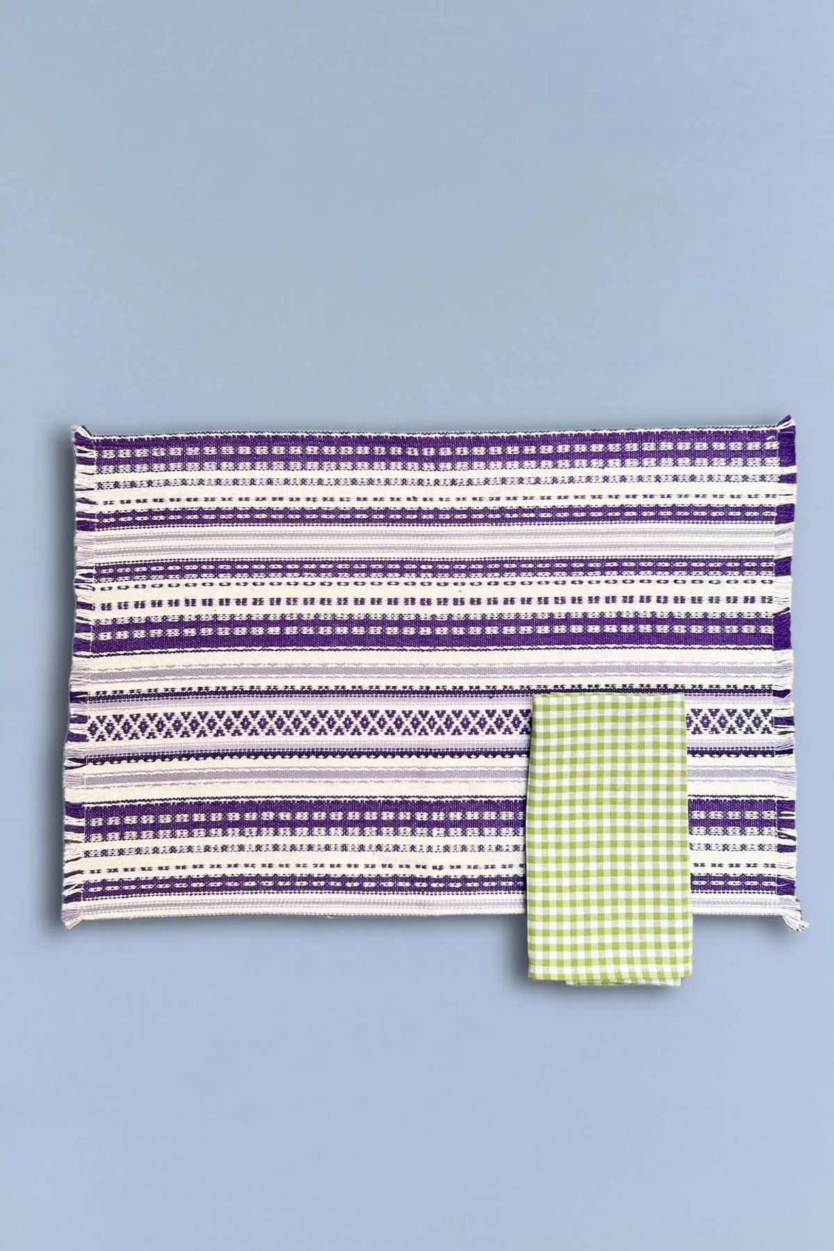 Mantel individual de algodón con estampado geométrico de rayas malva y blanco y una servilleta de cuadros verdes.