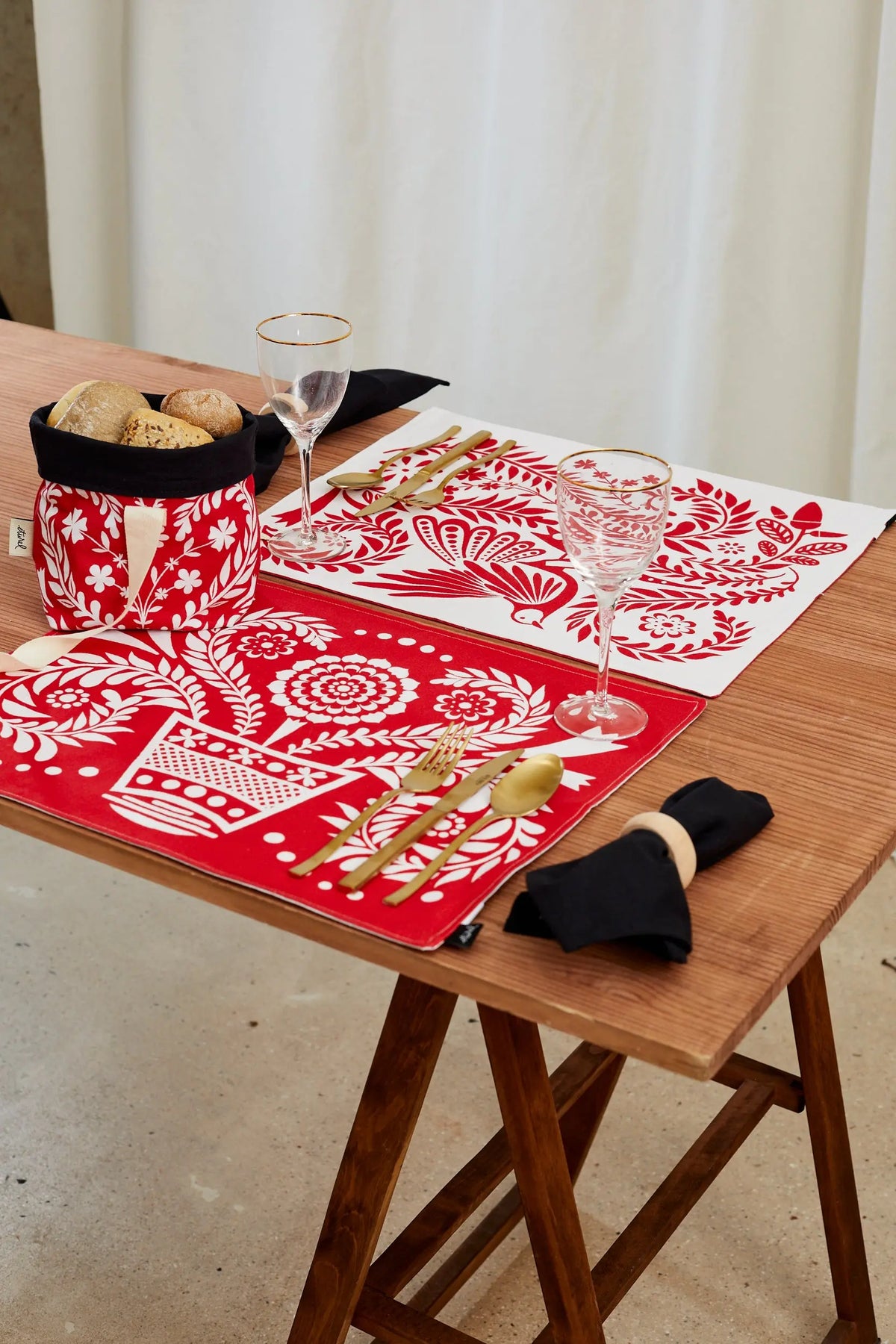 Pack de 2 manteles individuales reversibles con estampado folklore rojo y blanco sobre una mesa de madera.