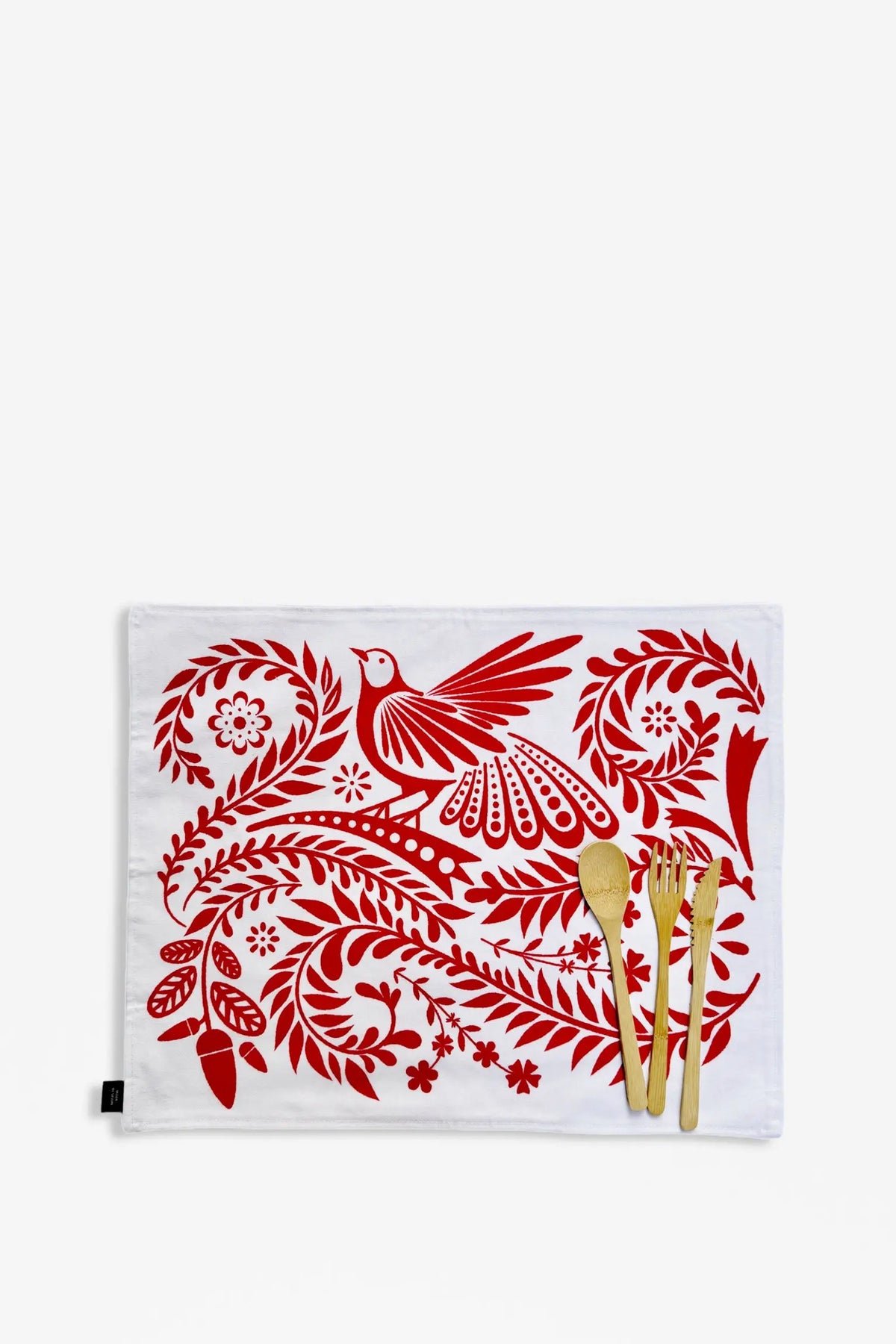 White rectangular placemat with red folklore bird and floral print, featuring bamboo spoon, fork, and knife set.