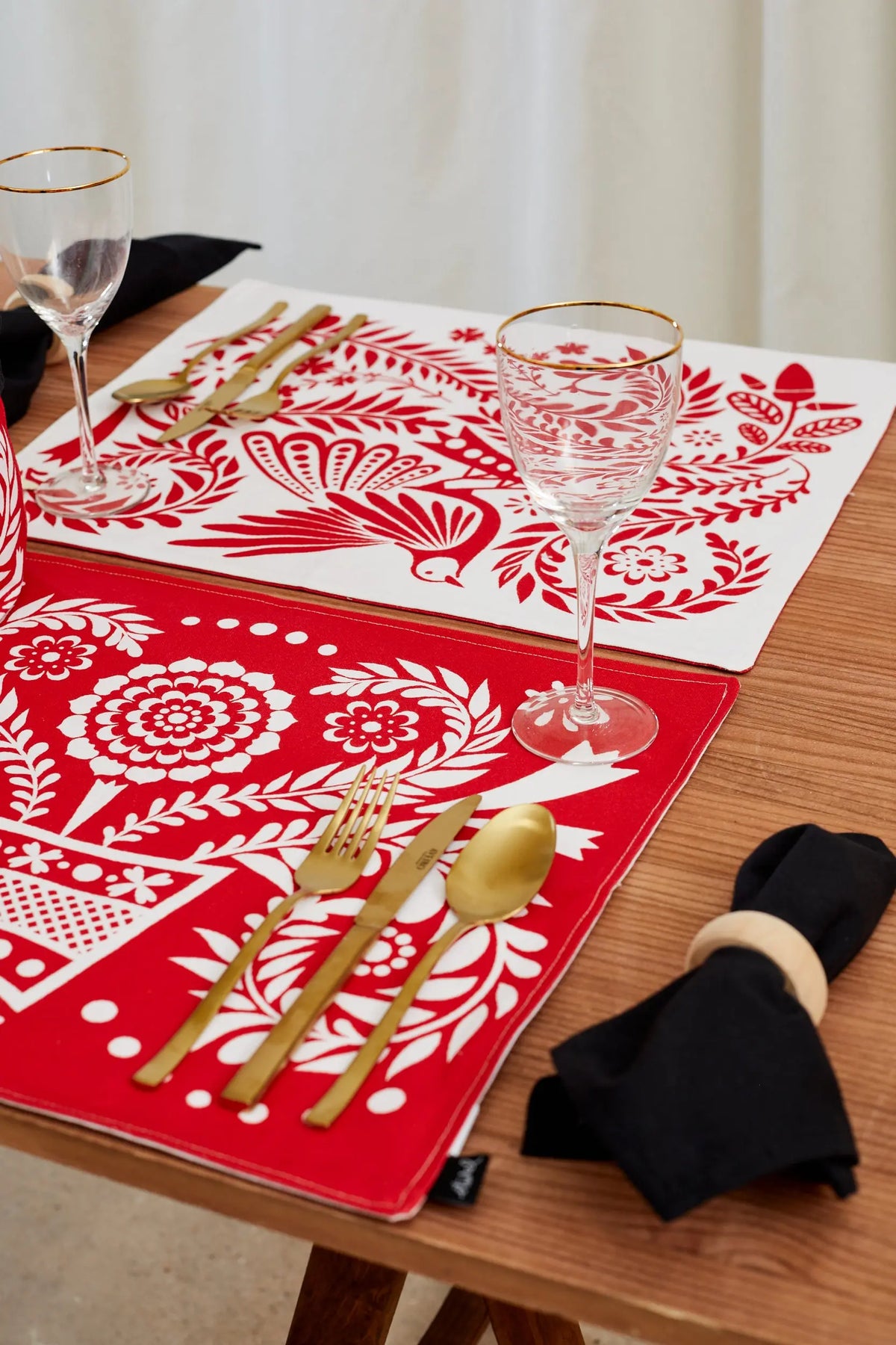 Pack de dos manteles individuales reversibles con estampado folclórico en blanco y rojo sobre una mesa de madera.