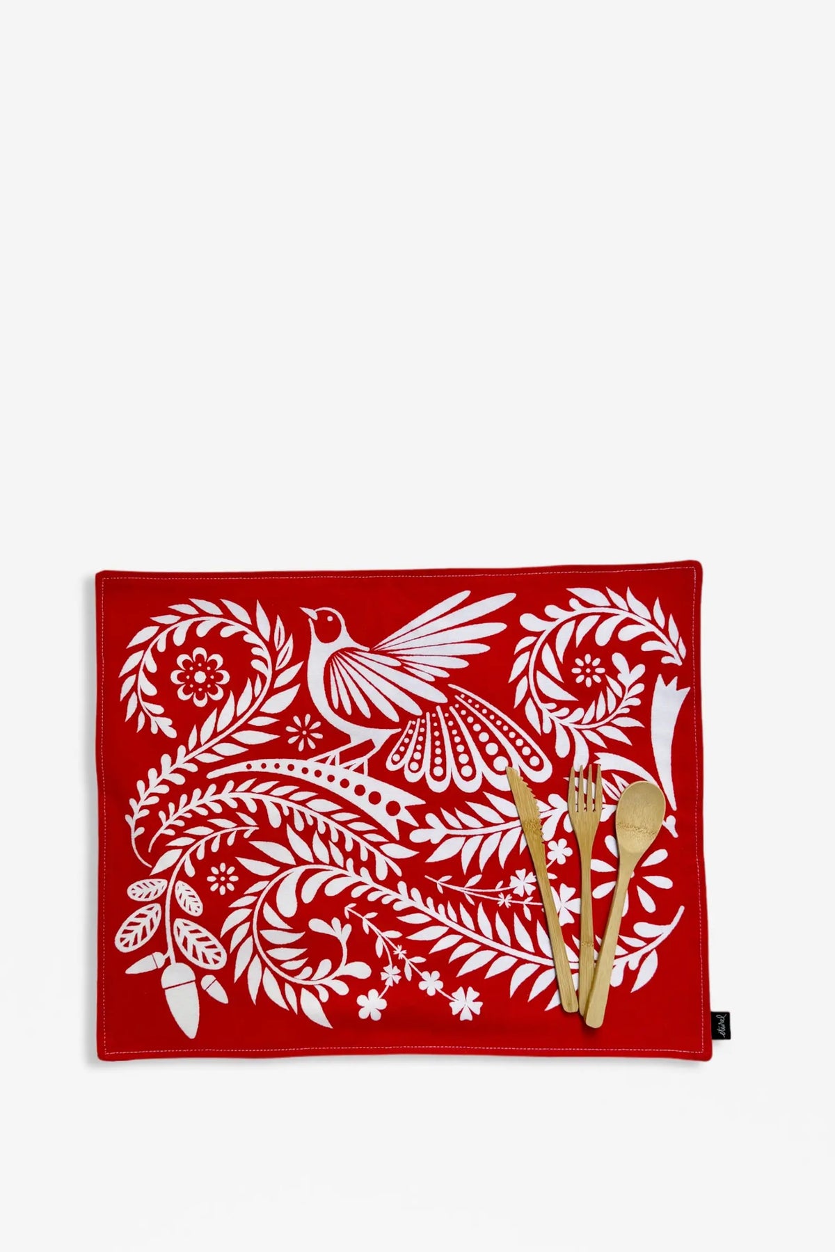 Mantel individual rojo con estampado de aves y flores blancas, estilo folclórico, sobre fondo blanco con cubiertos.