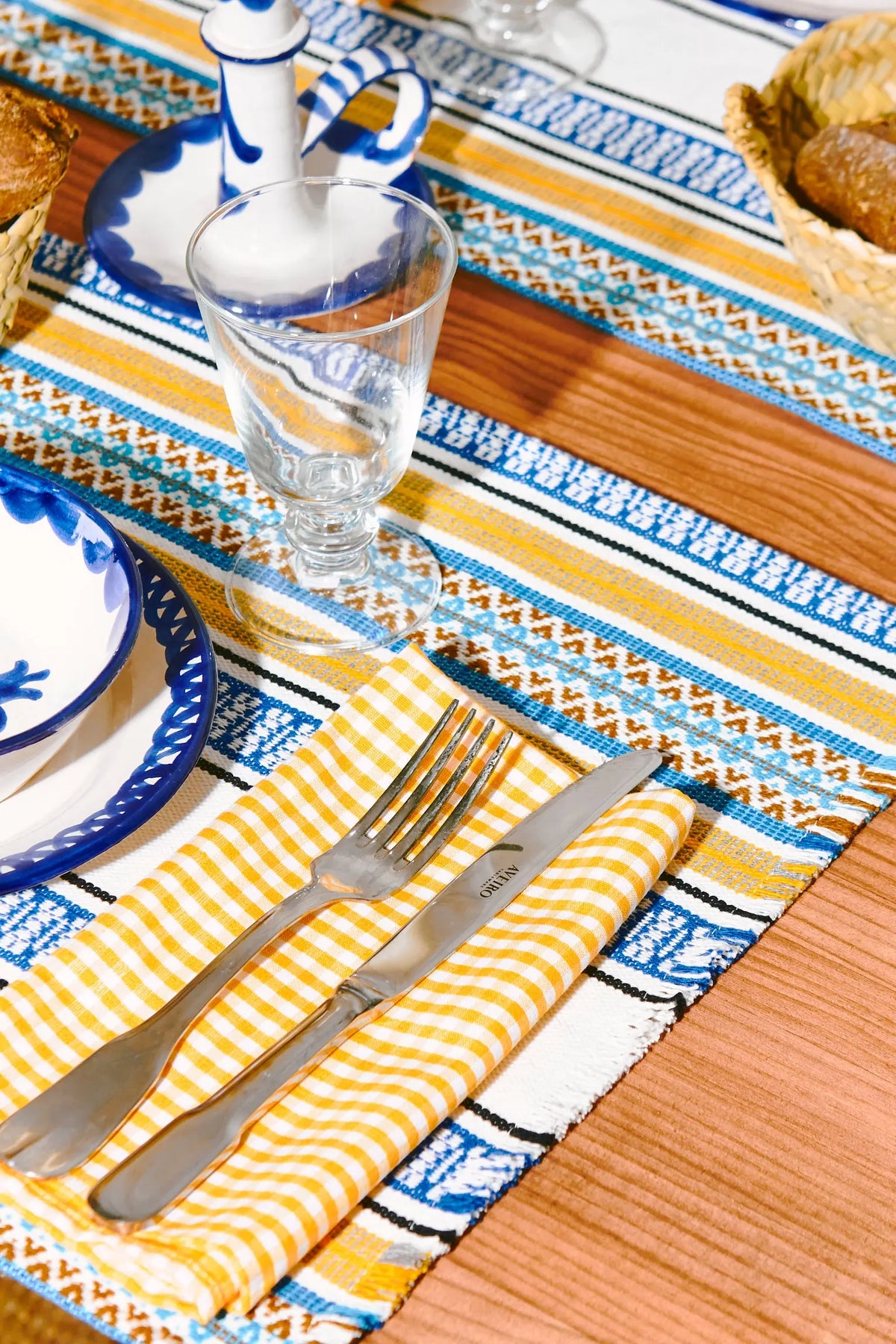 Dos manteles individuales de tela con rayas geométricas en tonos azul, amarillo y blanco, con bordes deshilachados.