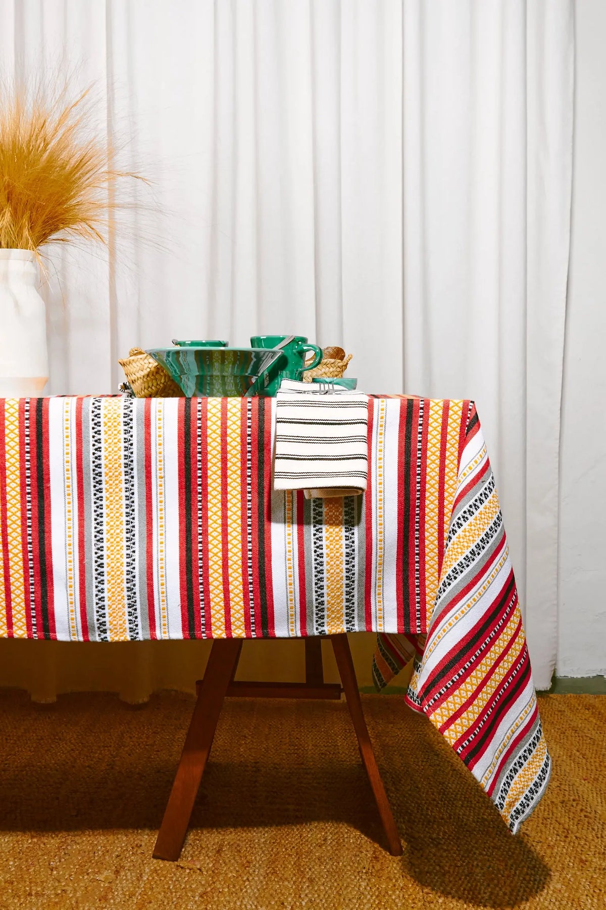 Mantel textil con rayas verticales en rojo, amarillo, blanco y negro, decorado con patrones geométricos tradicionales.