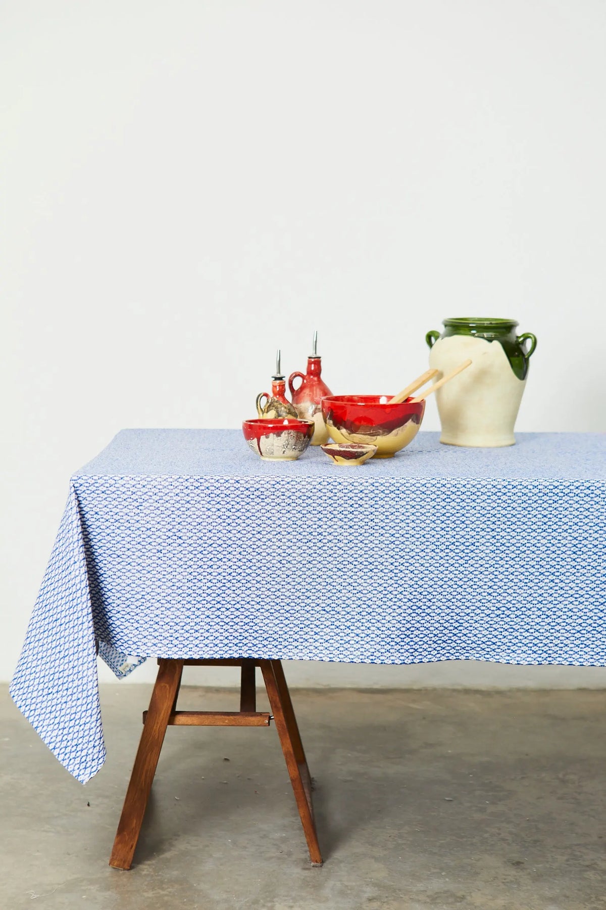 Mantel azul con patrón geométrico tipo ojo de perdiz sobre una mesa de madera con vajilla artesanal de cerámica.
