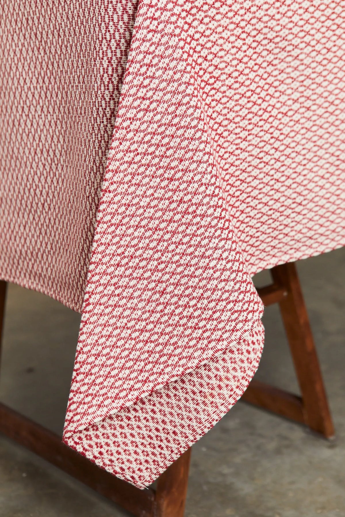 Mantel granate con patrón tejido ojo de perdiz sobre una mesa de madera, elegante textura geométrica bicolor.