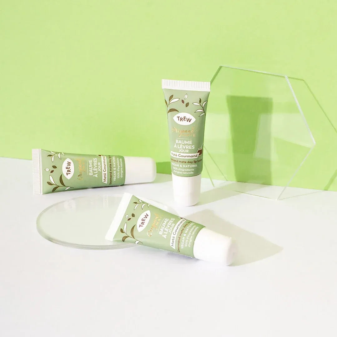 Three tubes of Trew lip balm in pale green packaging with botanical motifs, displayed on clear acrylic stands.