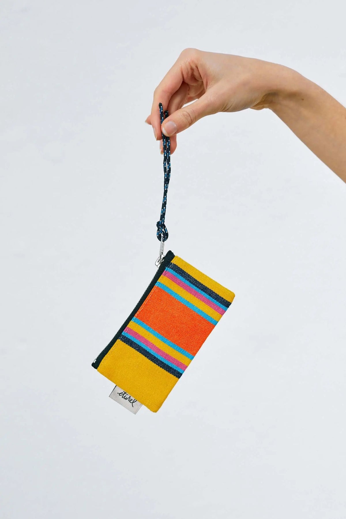 Yellow striped canvas coin purse with a blue rope handle, held by a hand against a white background.