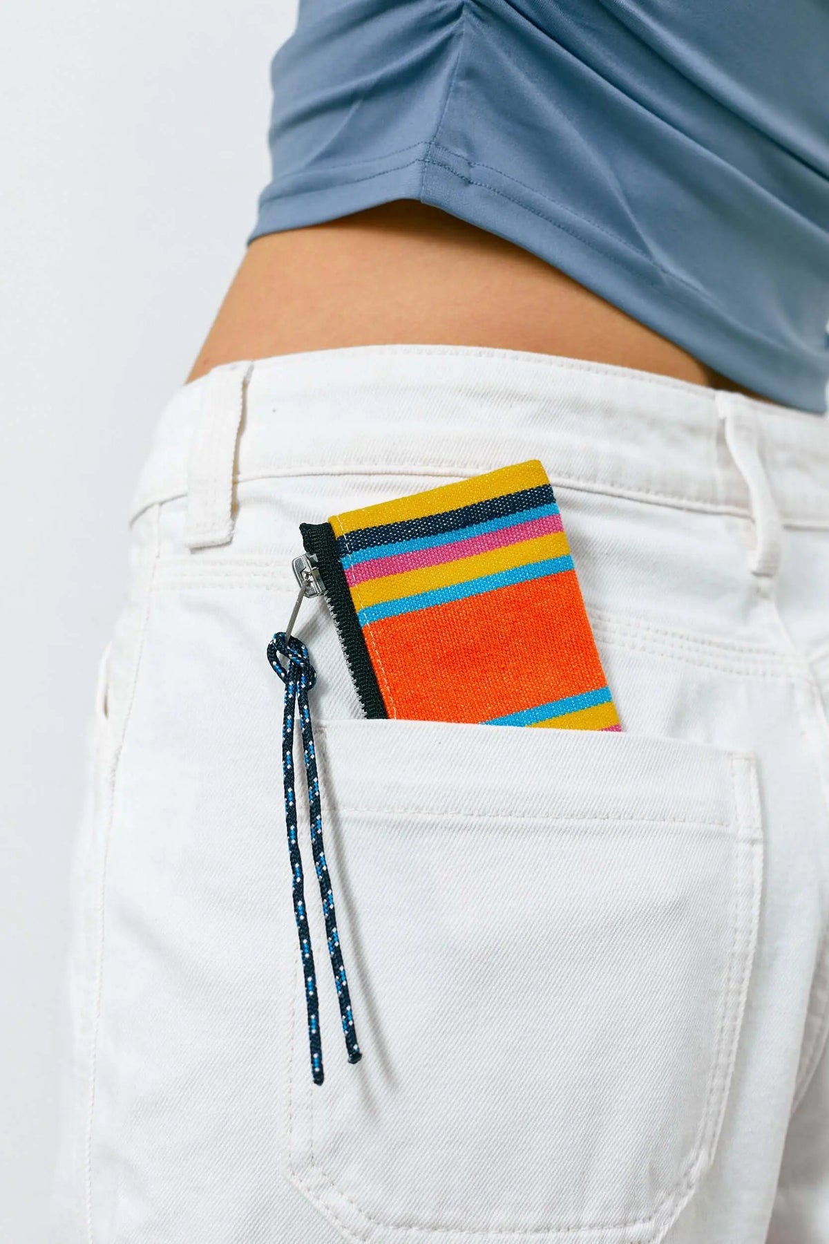 Yellow, orange, and blue striped canvas coin purse with a black zipper and cord pull, inside a white jeans pocket.