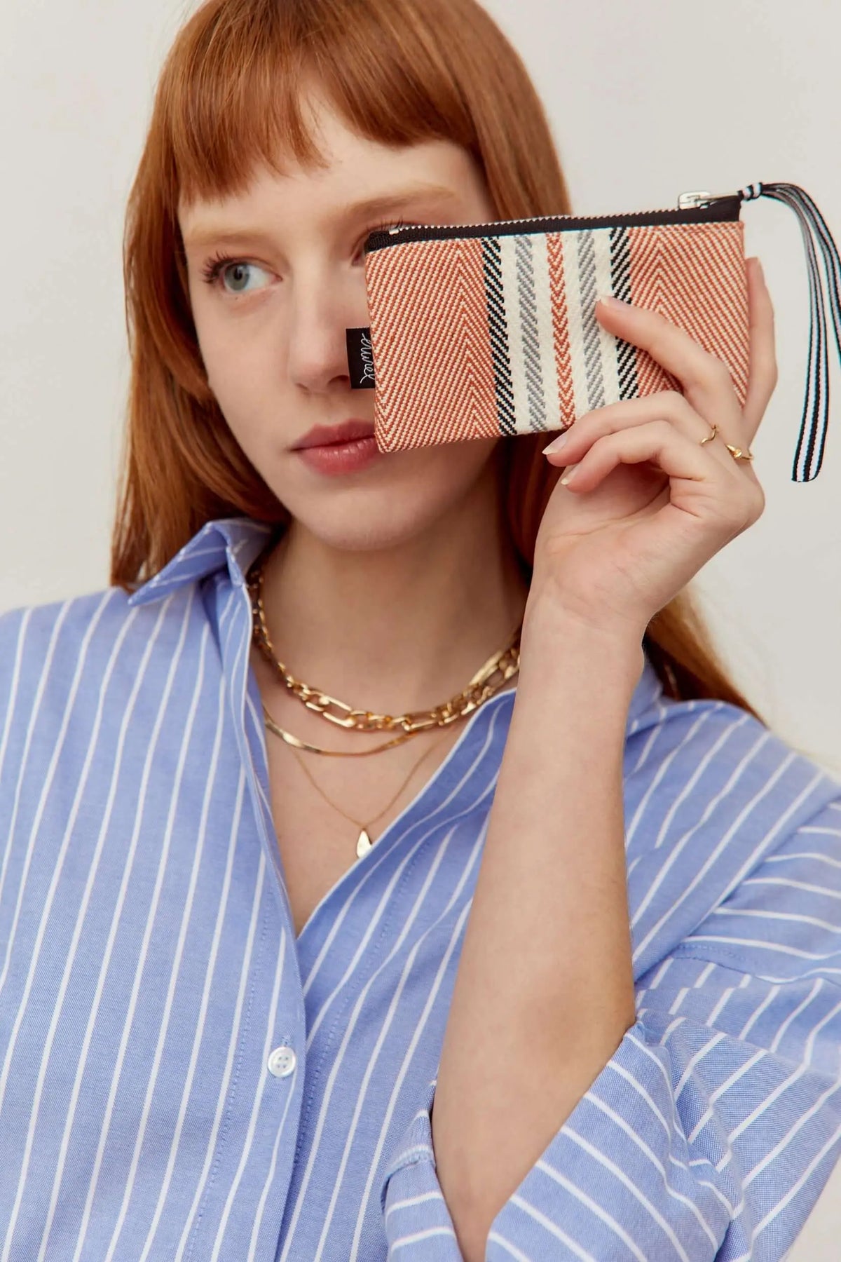 Small rectangular coin purse in terracotta, white, and black striped woven fabric with a matching wrist strap.
