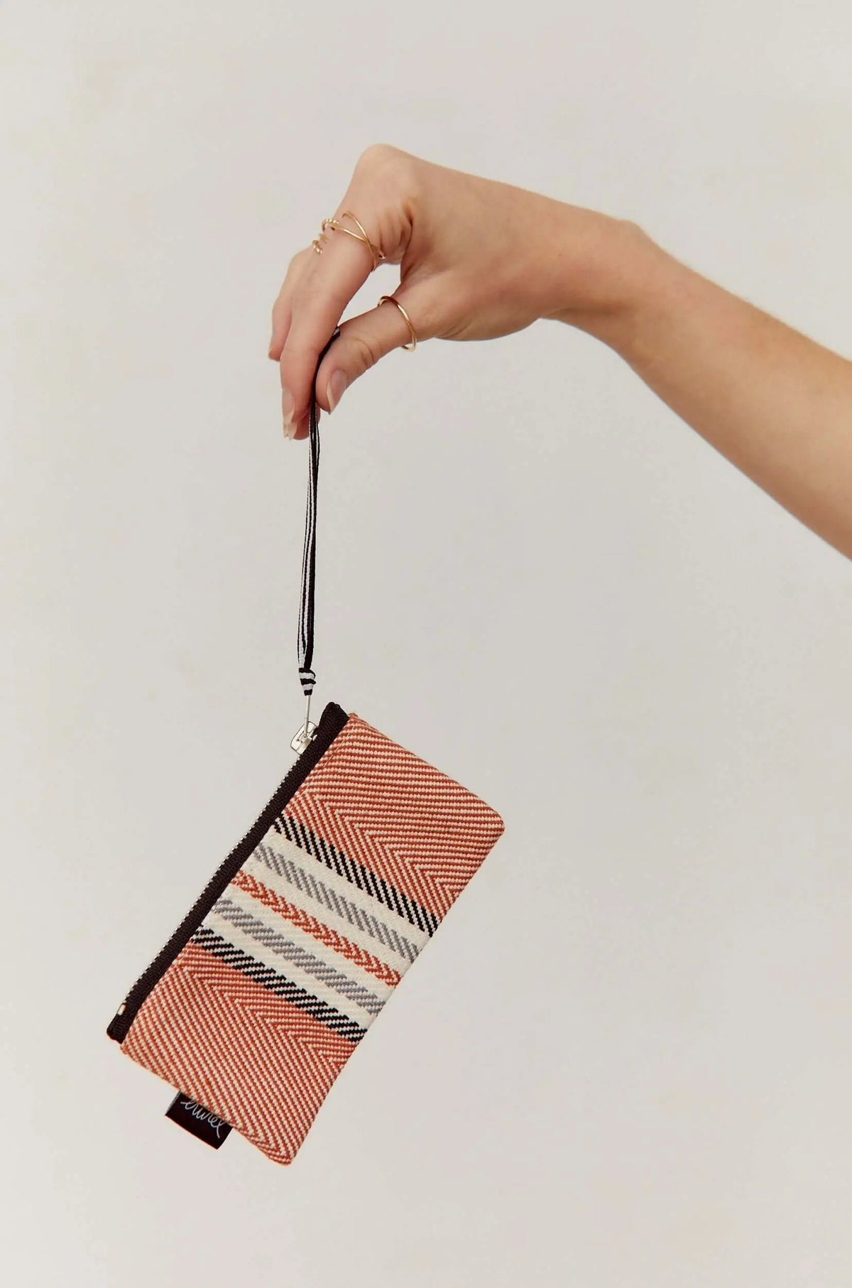 Monedero rectangular de tejido sarga color arcilla con patrón de espiga, cremallera y asa de mano a rayas.