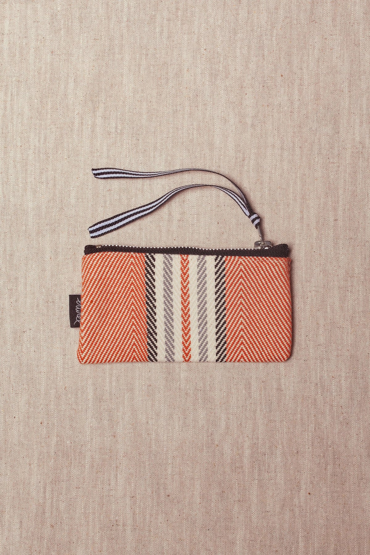 Rectangular coin purse in clay-colored herringbone fabric with central striped pattern and a black-and-white wrist strap.