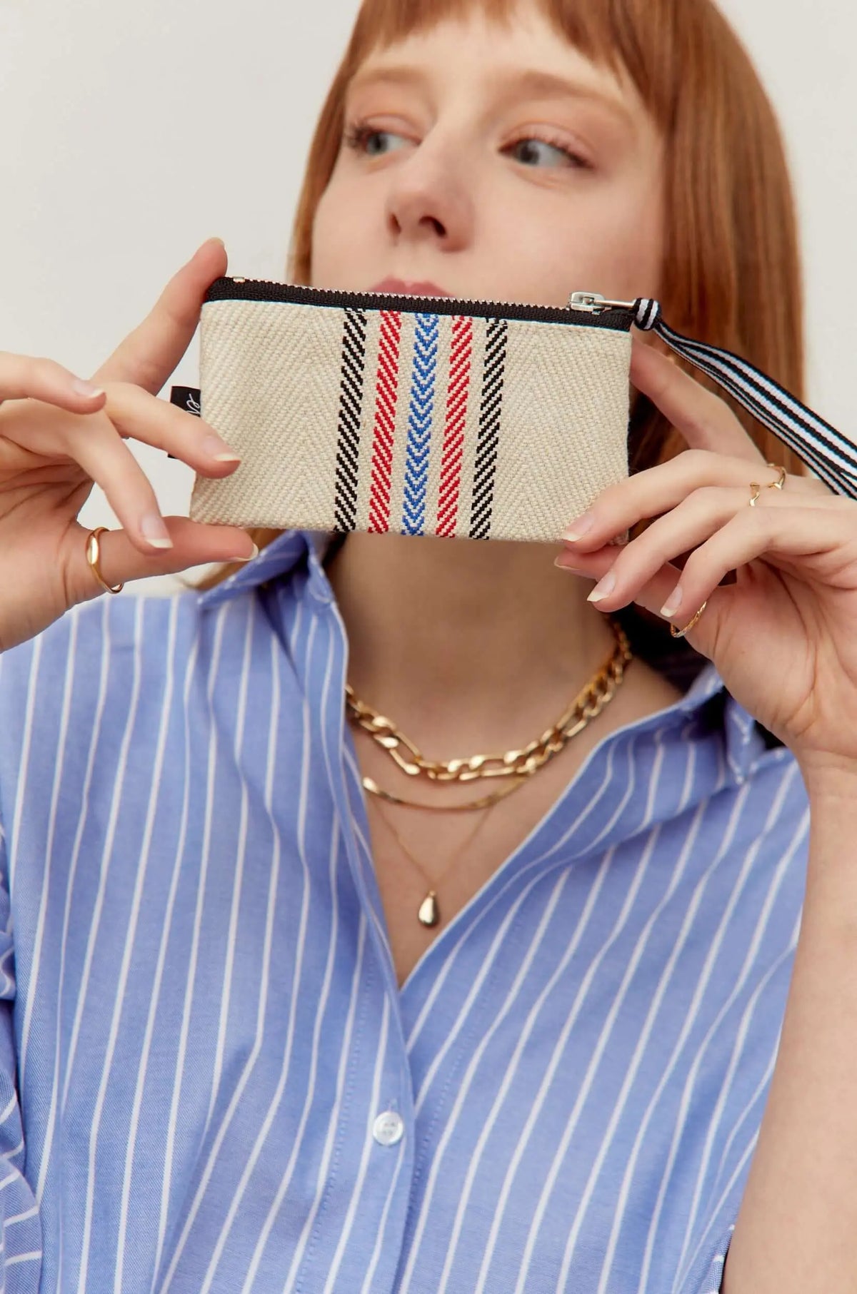 Cream twill coin purse with red, blue, and black chevron stripes, black zipper closure, and a matching wrist strap.