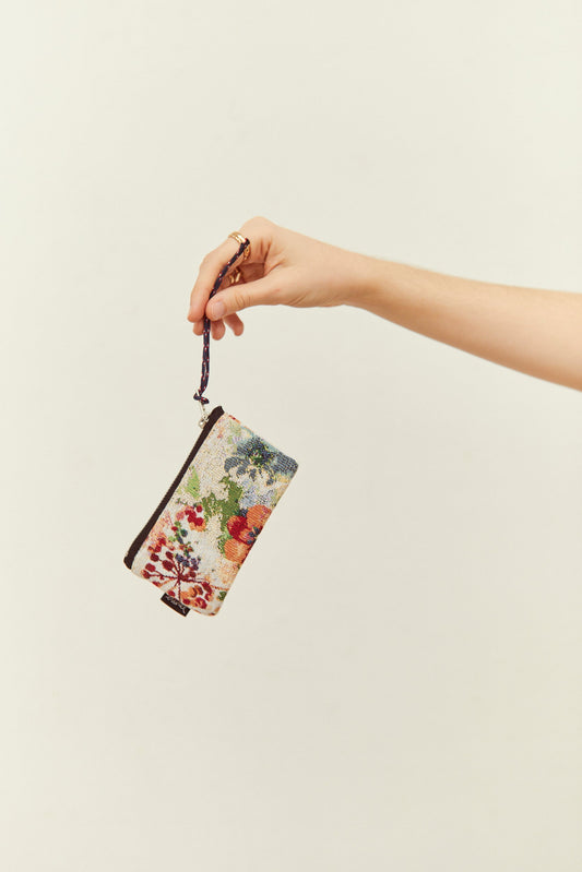 Monedero de tela jacquard con estampado de amapolas y flores, con correa de mano, sostenido por una mano.