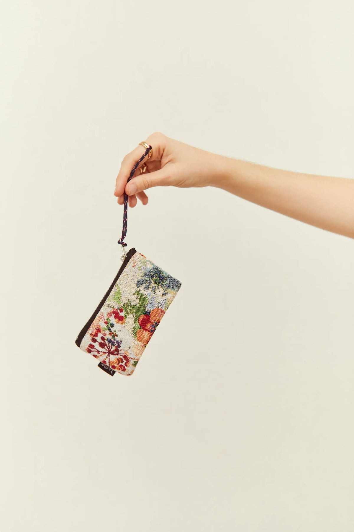 Monedero de tela jacquard con estampado de amapolas y flores, con correa de mano, sostenido por una mano.