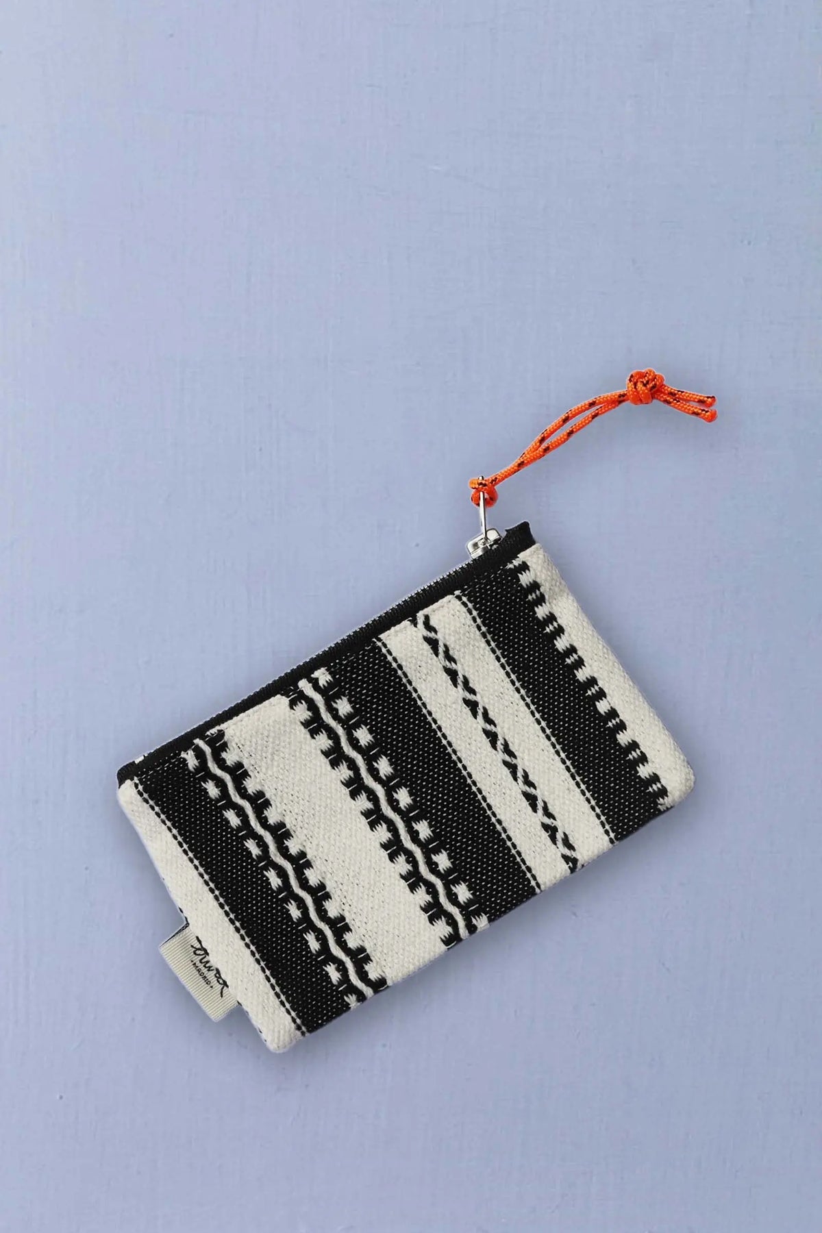 Monedero de tejido alpujarreño en blanco y negro, con cremallera y tirador de cuerda naranja sobre fondo azul claro.