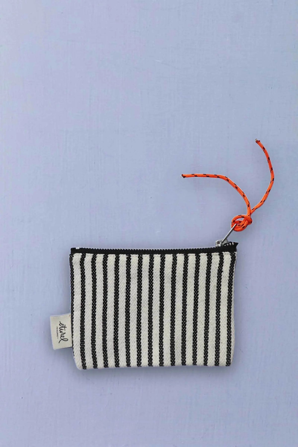 Monedero de loneta con rayas verticales negras y blancas, cremallera superior y tirador de cuerda naranja anudada.