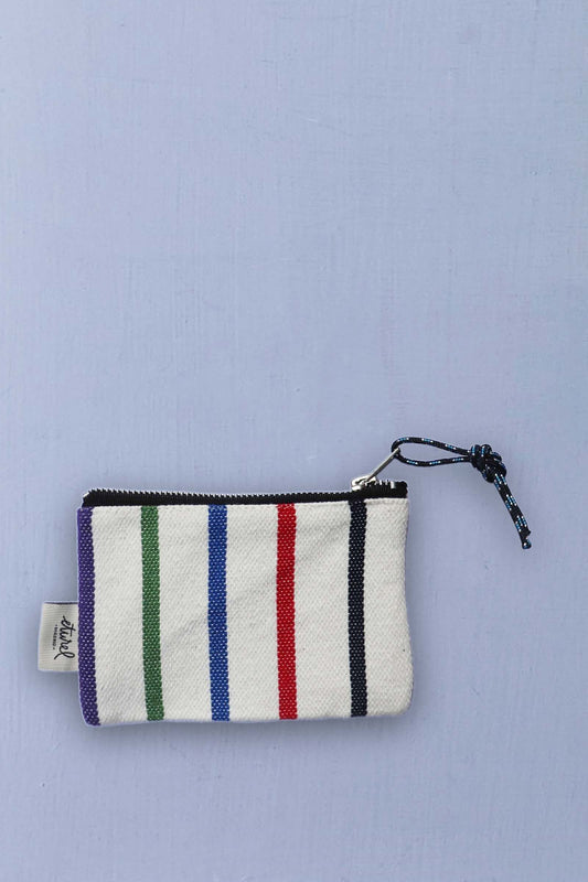 Monedero de tela blanca con rayas verticales de colores, cierre de cremallera y tirador de cuerda sobre fondo lila.