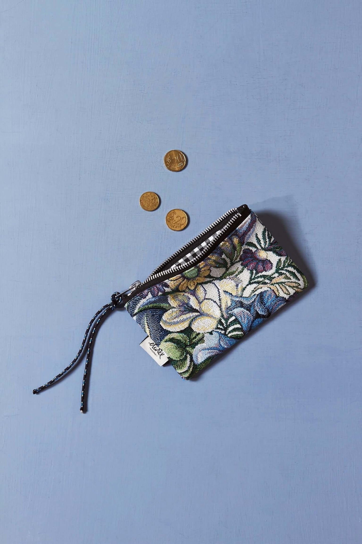 Monedero de tejido jacquard con estampado de flores azules sobre fondo celeste, cierre de cremallera y tres monedas.