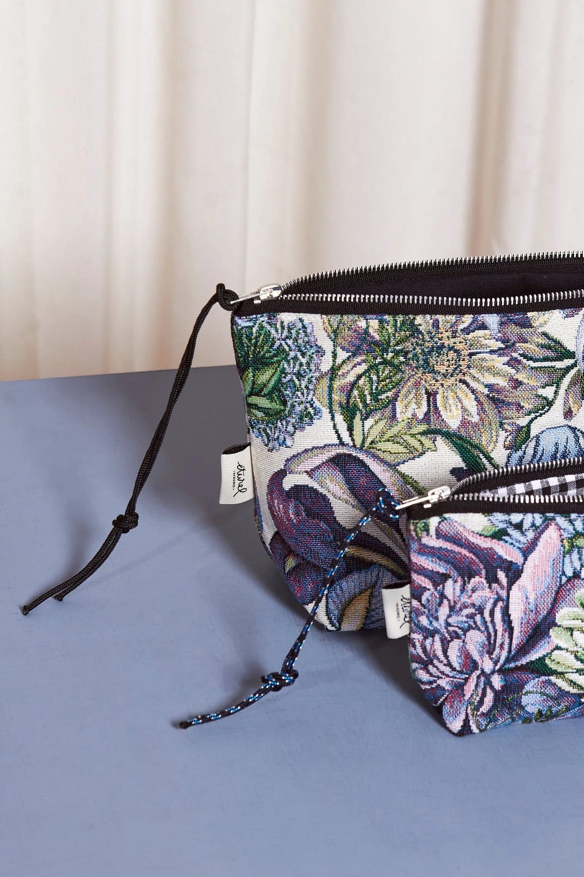 Neceser y estuche de tela jacquard con estampado de crisantemos azules y verdes, cierre de cremallera y tirador negro.
