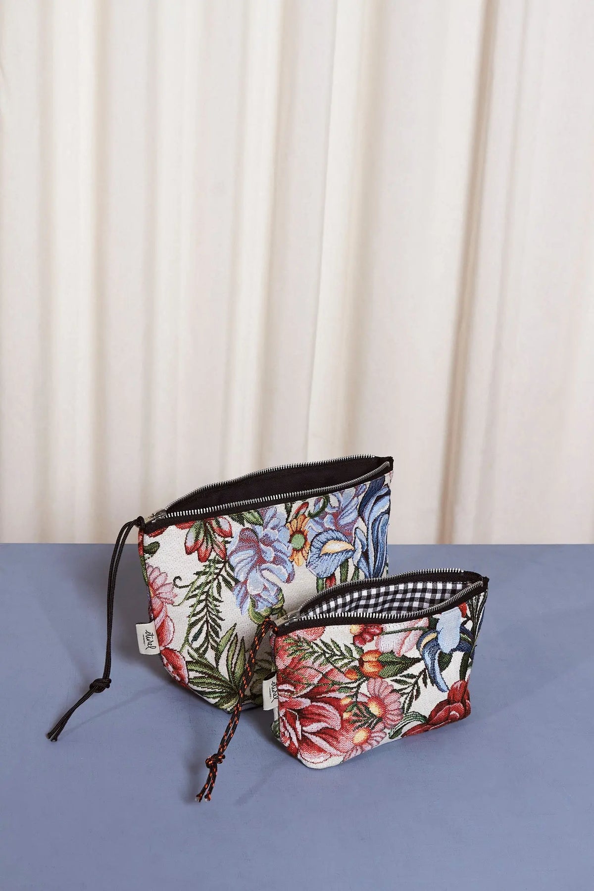 Dos neceseres de tela jacquard con estampado de flores rojas y hojas, cierre de cremallera y forro interior.