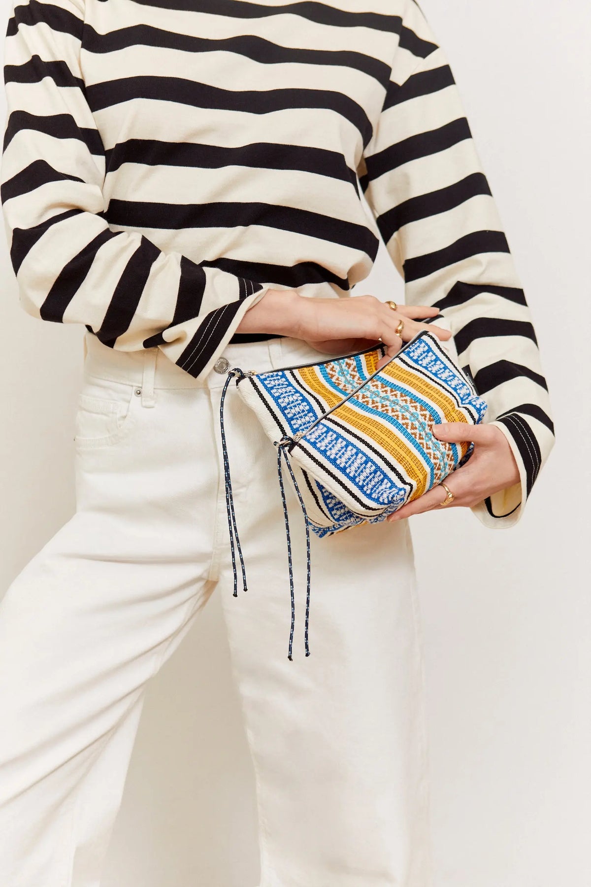Blue, yellow, and white woven fabric pouch with patterned stripes and dangling cord pull tabs held by a person.