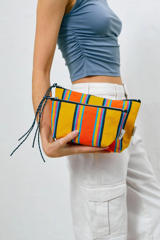 A person holds two yellow, orange, and blue striped canvas pouches with matching rope zipper pulls.