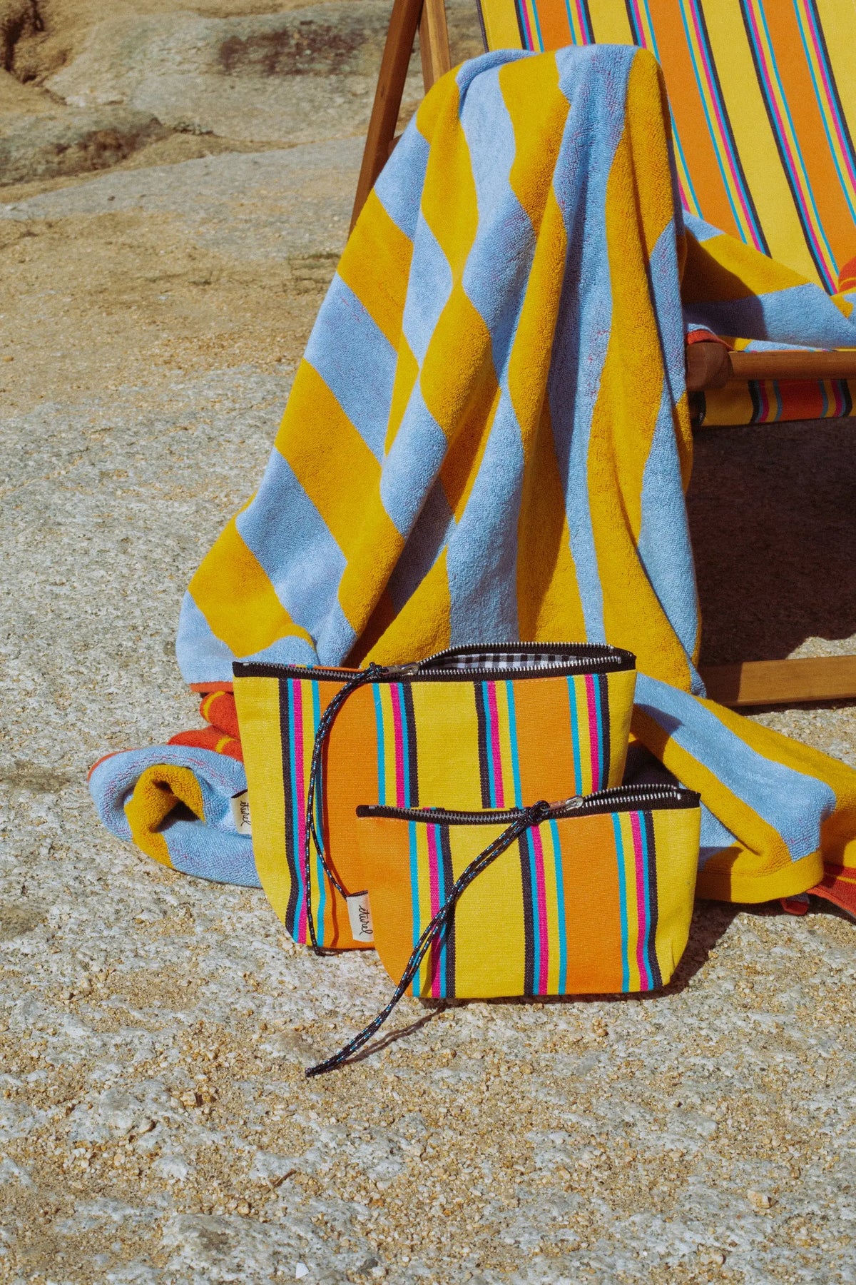 Two yellow and orange striped canvas pouches with zip closures, placed on a beach chair with a matching towel.