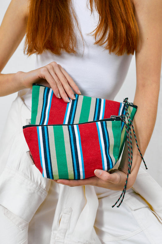 Neceser de lona estilo hamaca con rayas coloridas en rojo, verde y azul, con cremallera y cordones decorativos.