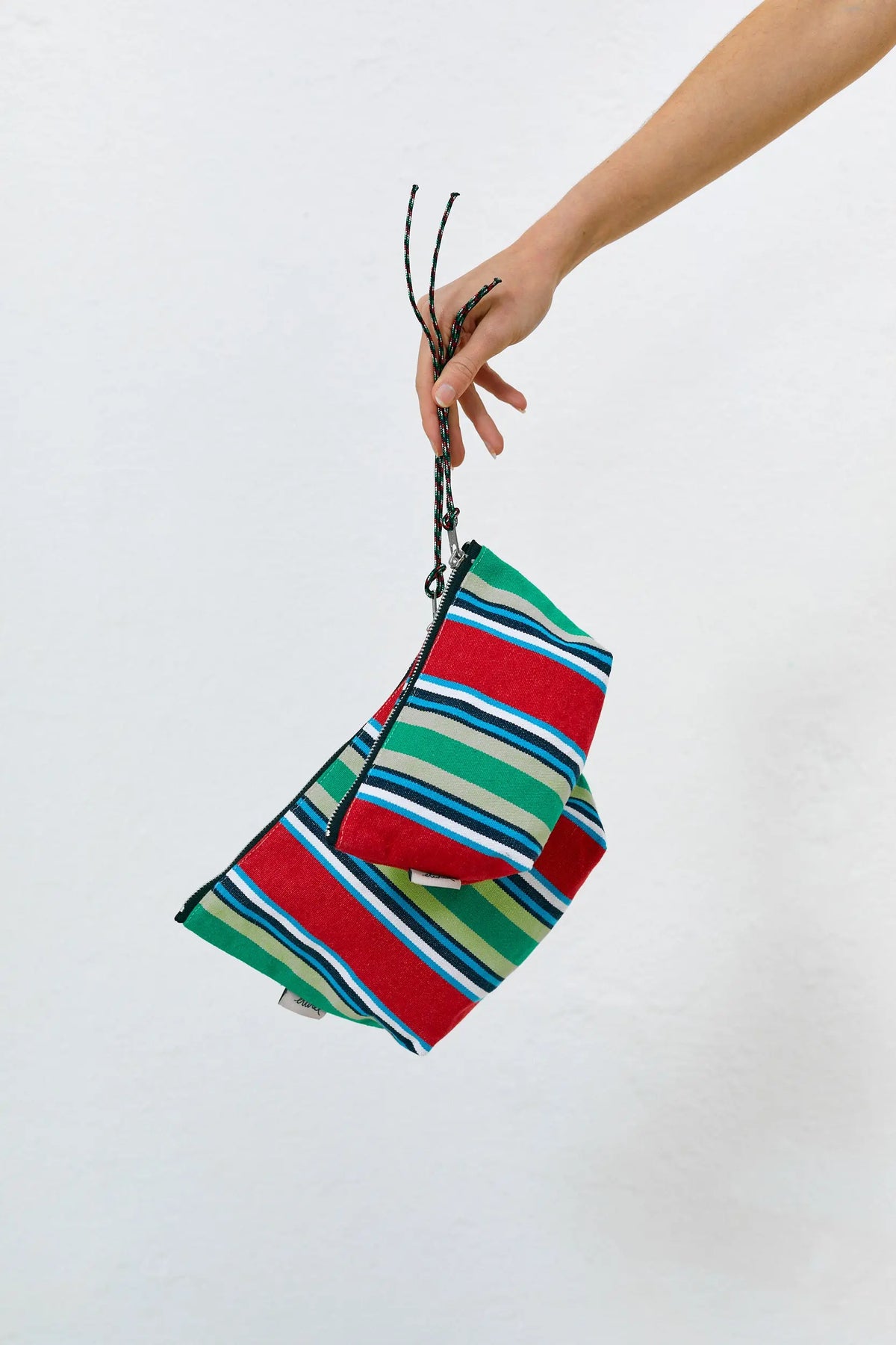 Hand holding two red, green, and blue striped canvas pouches with zip closures and patterned cord pulls.
