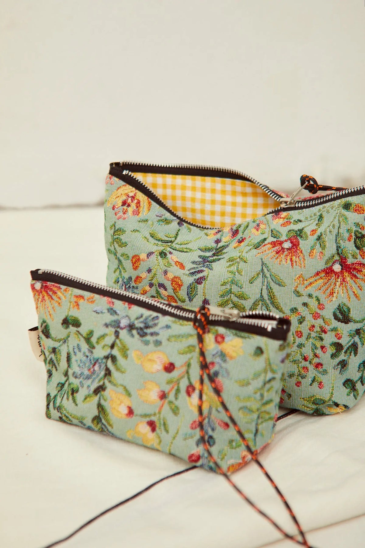 Dos neceseres de tela jacquard en verde claro con estampado de flores azaleas y forro interior a cuadros amarillos.