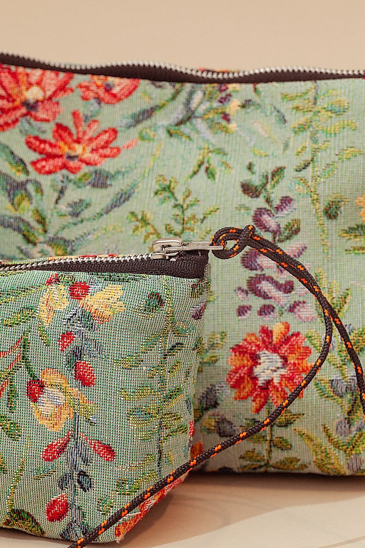 Light blue jacquard fabric toiletry bags with vibrant red and yellow azalea floral pattern and black cord zip pulls.