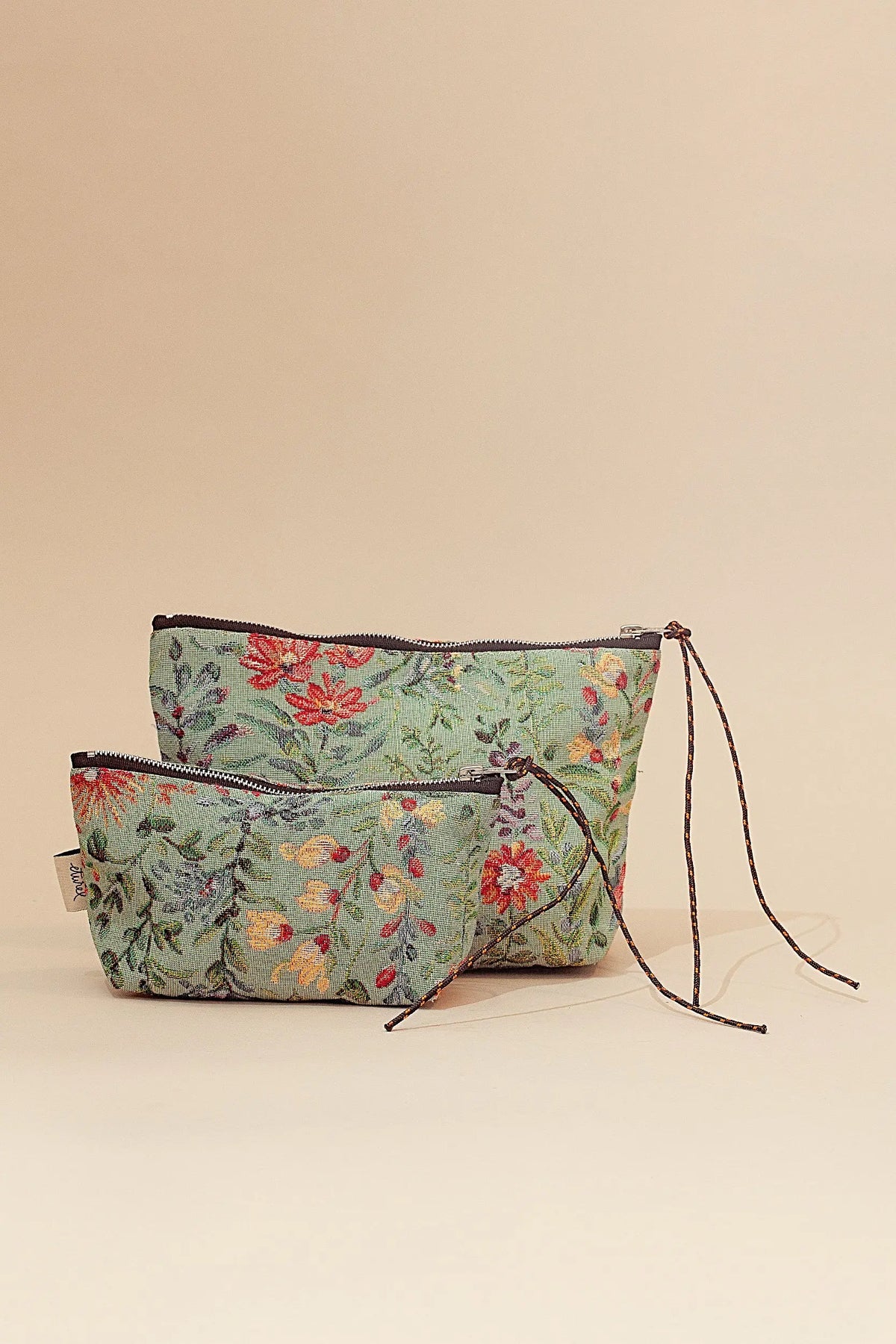 Set de dos neceseres de tela jacquard en tono celeste con estampado floral multicolor y cierre de cremallera con cordón.